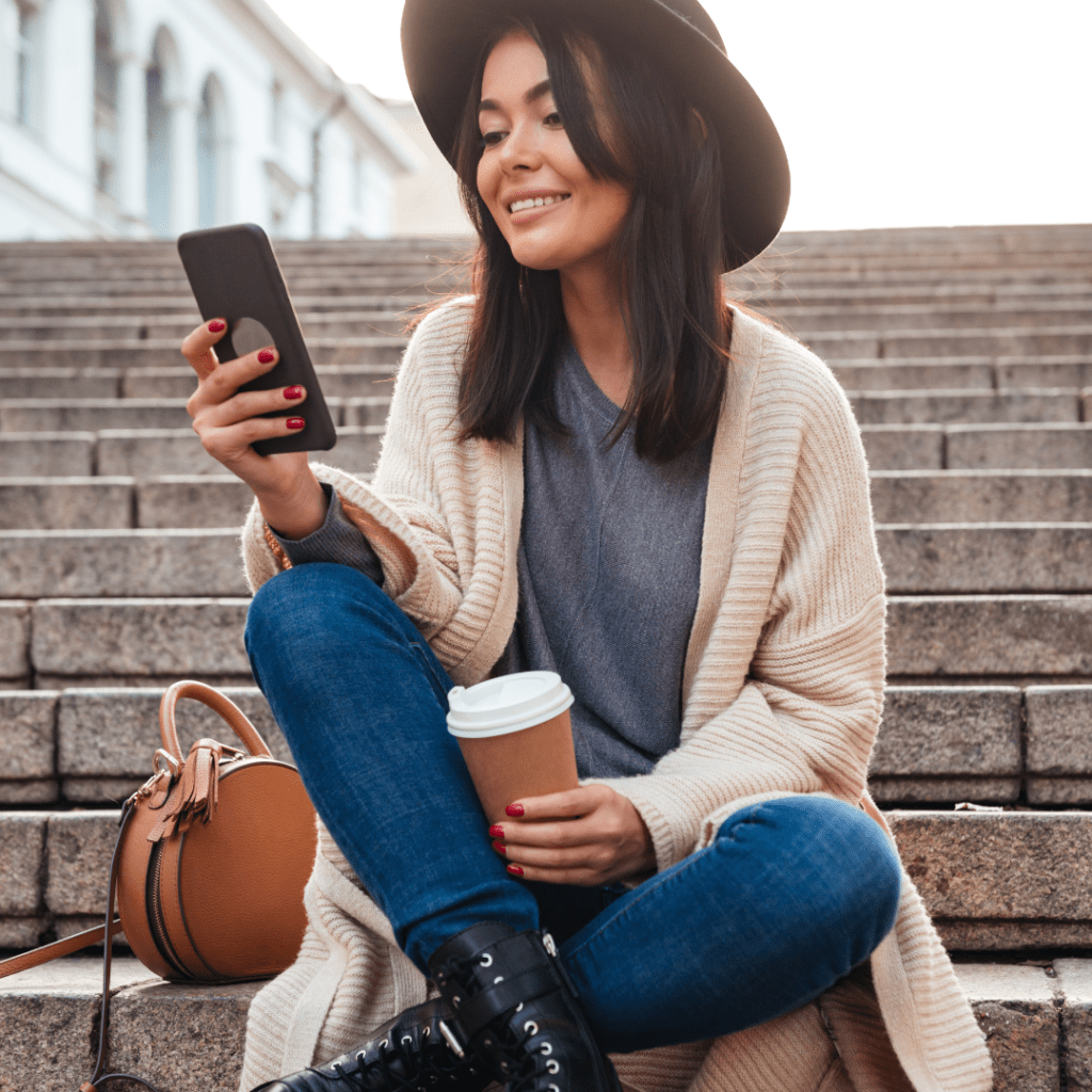 woman sitting on steps holding coffee and phone