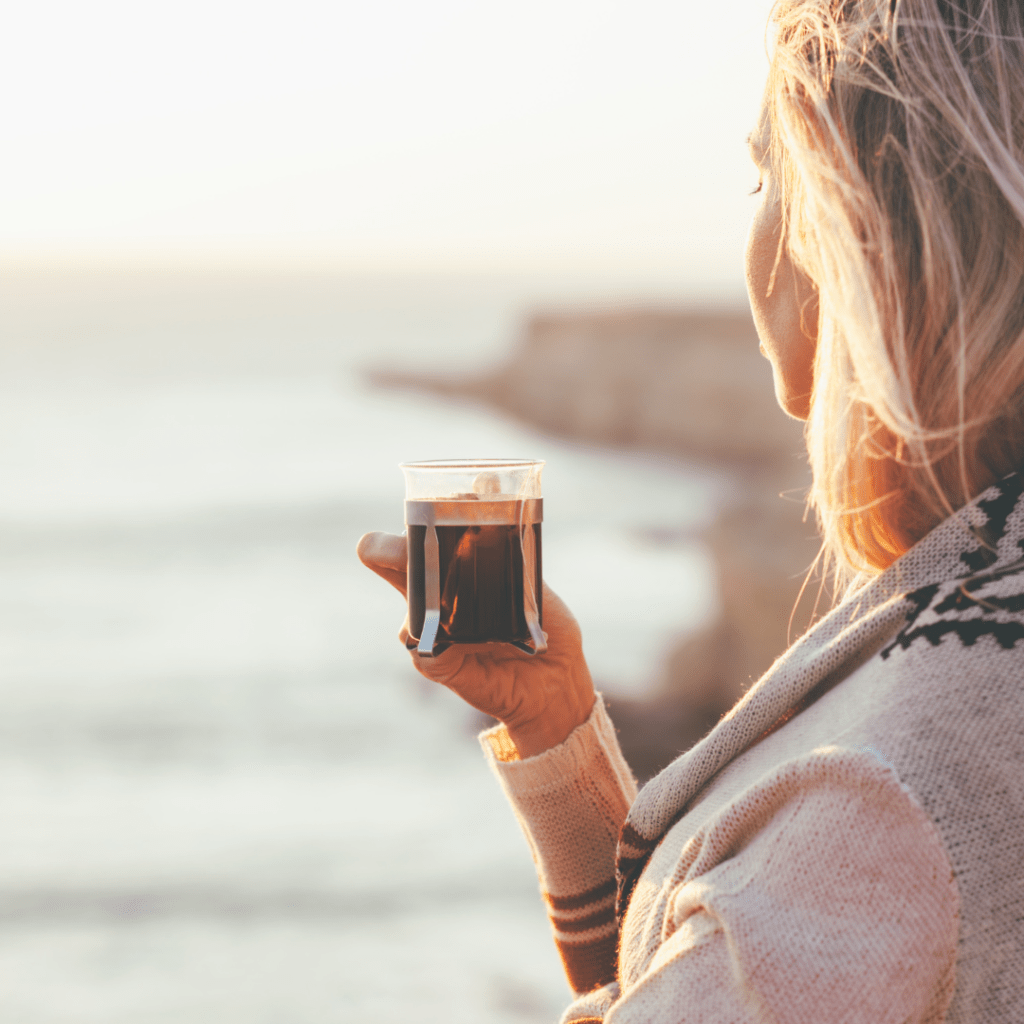 blonde woman standing on beach holding coffee