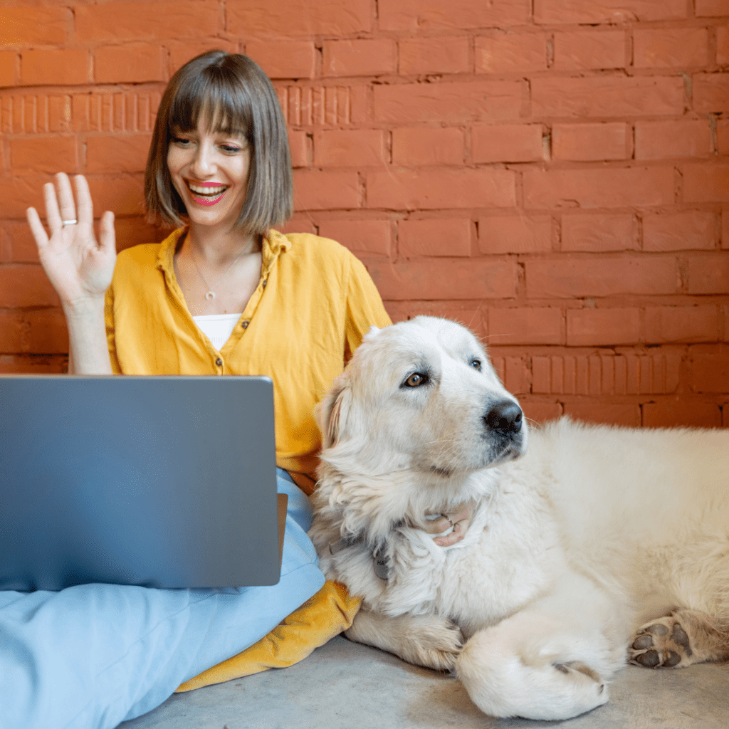 woman on laptop next to dog waving